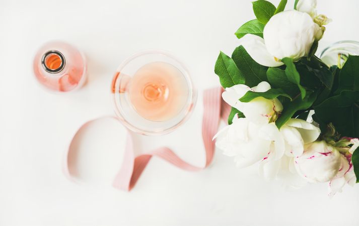 Top view of glass of pink rose wine, and bottle with flowers and ribbon, horizontal composition