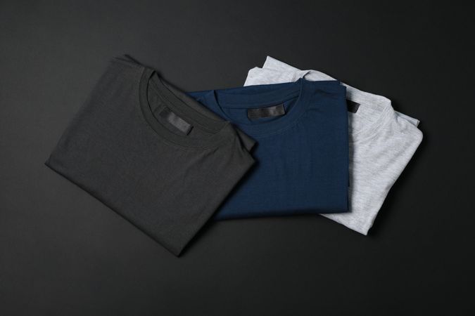 Folded multicolored t-shirts on dark background, space for text
