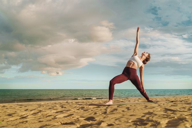Woman Practicing Yoga on Beach - Serene Stretching Pose by Ocean at Sunset