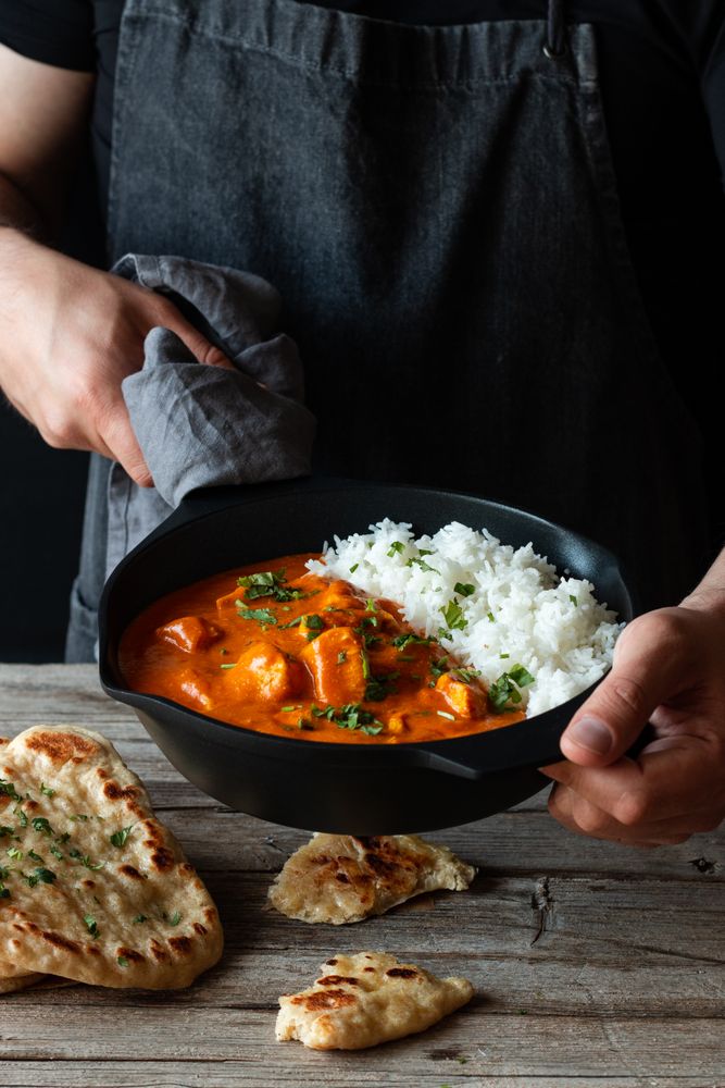 Faceless cook holding frying pan with hot butter chicken