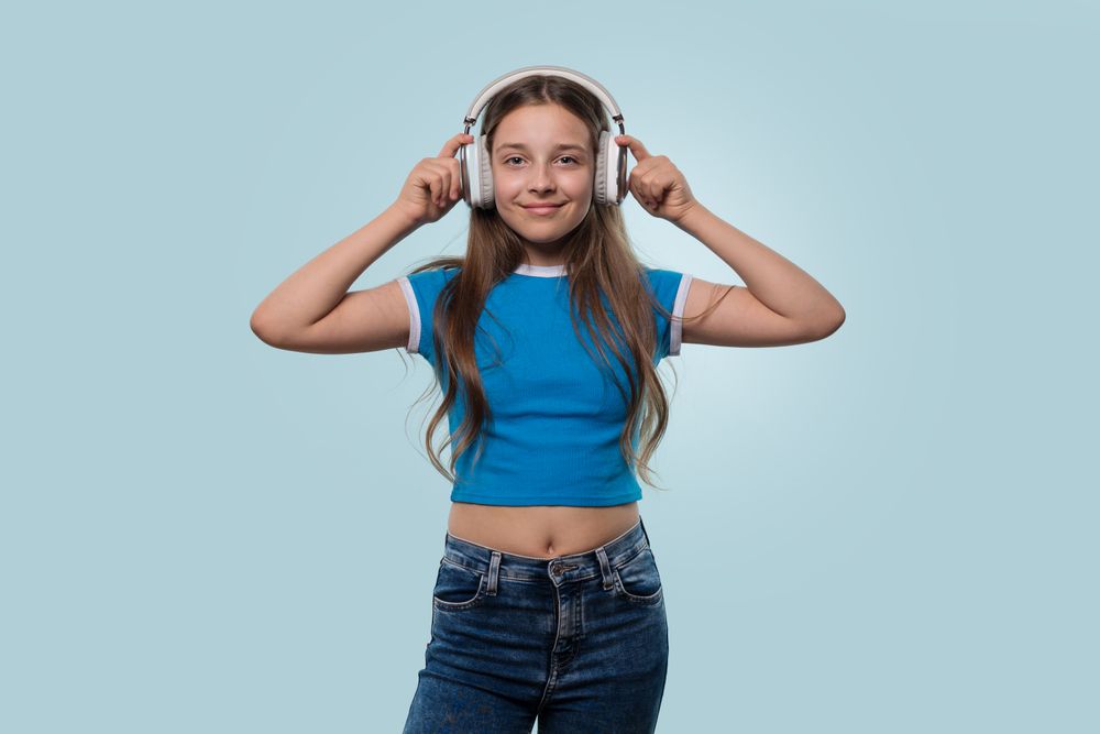 Young girl wearing headphones, smiling while adjusting them.