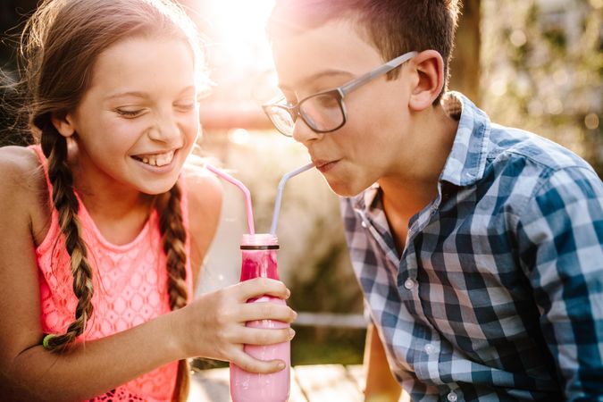 Boy and girl in love sharing a smoothie using two straws sitting outdoors