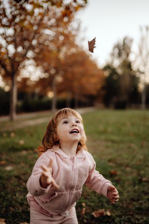 Joyful child scattering leaves on lawn in park