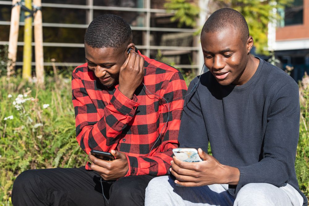 Positive Black men using smartphones together in park