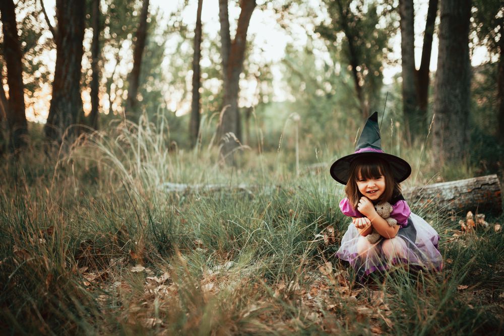 Girl in witch costume crouched down in the forest