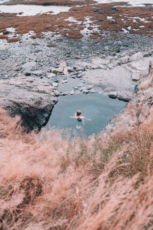 Woman in pond near hill on shore