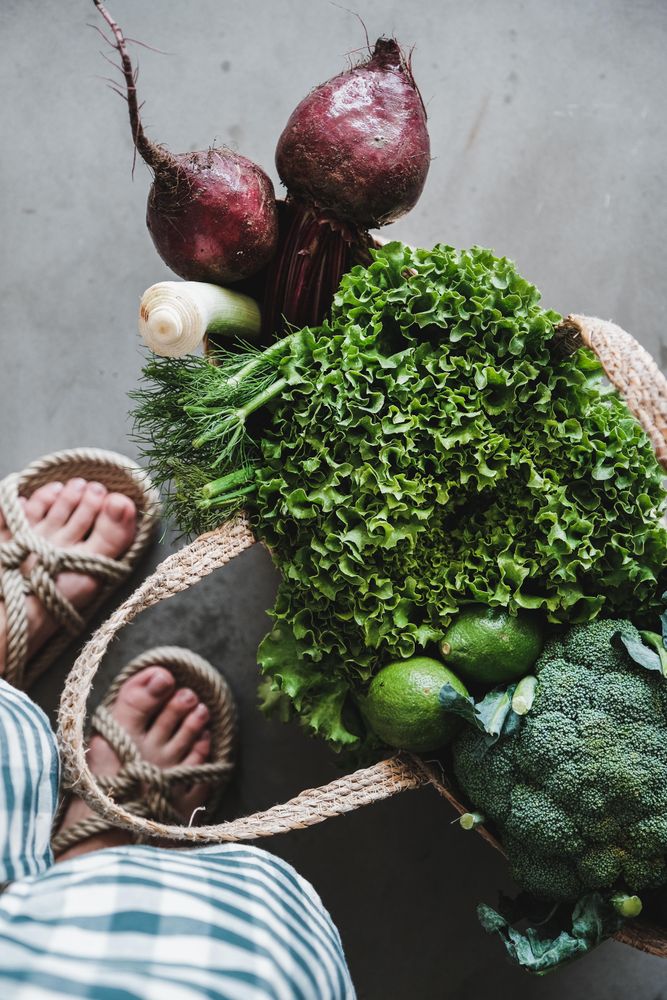 Overhead shot of grocery shopping jute full of fresh produce, with feet, vertical composition