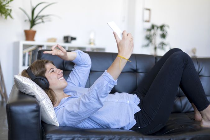 Woman relaxing on a sofa taking selfie on her phone