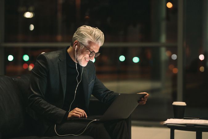 Smiling mature businessman working late on laptop in office lobby