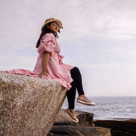 Woman in pink long sleeve shirt sitting on rock on seashore
