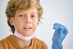 Crop nurse with swab touching face of crying boy
