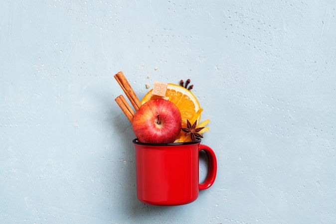 Mulled wine in ingredients in red ceramic mug on frosted blue background
