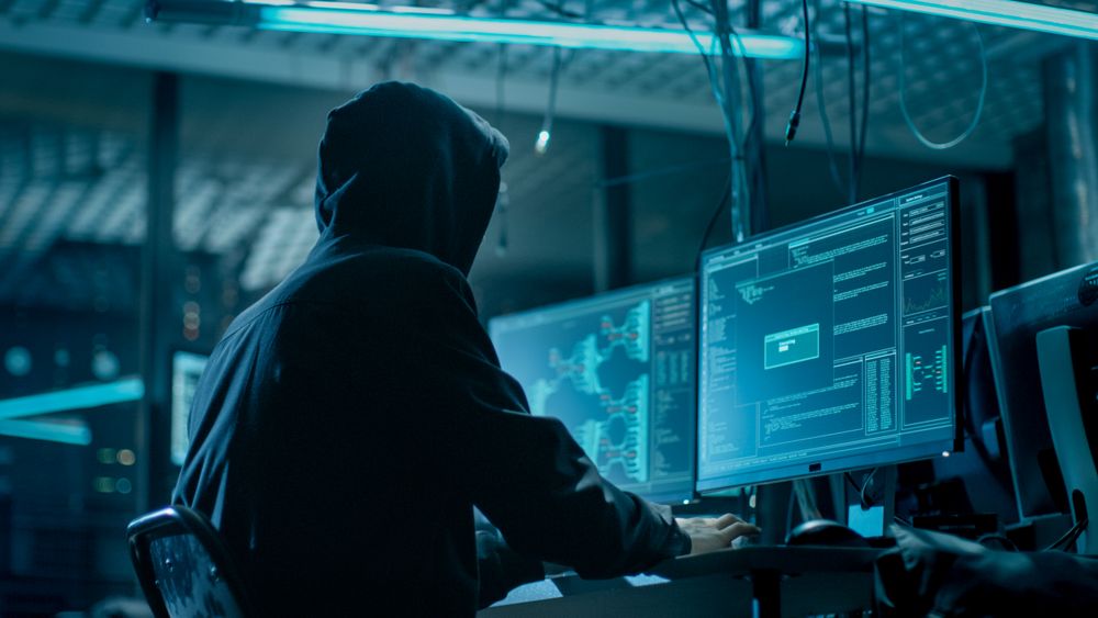 Shot from the Back to Hooded Hacker Breaking into Corporate Data Servers from His Underground Hideout.