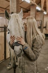 Woman hugging horse with long mane in face in stable