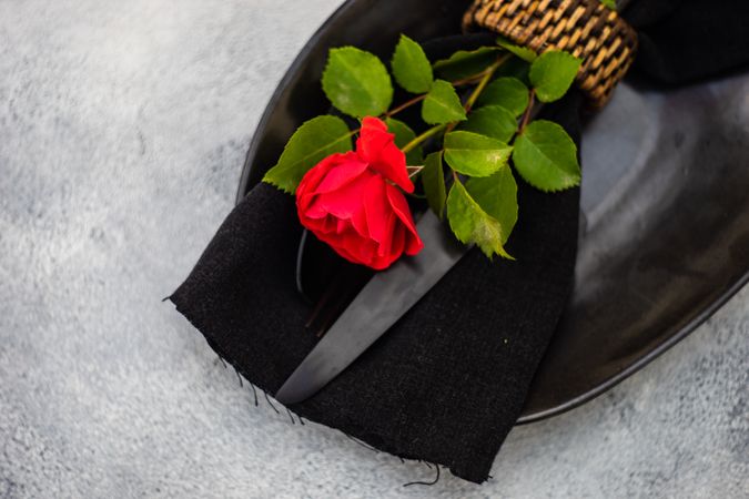 Top view of table setting with red rose on dark plate