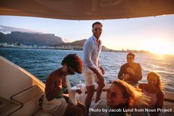 Smiling male standing on back of yacht while friends laugh 0gj98b