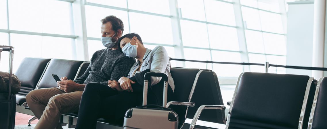 Man and woman with face masks sitting at airport terminal waiting lounge