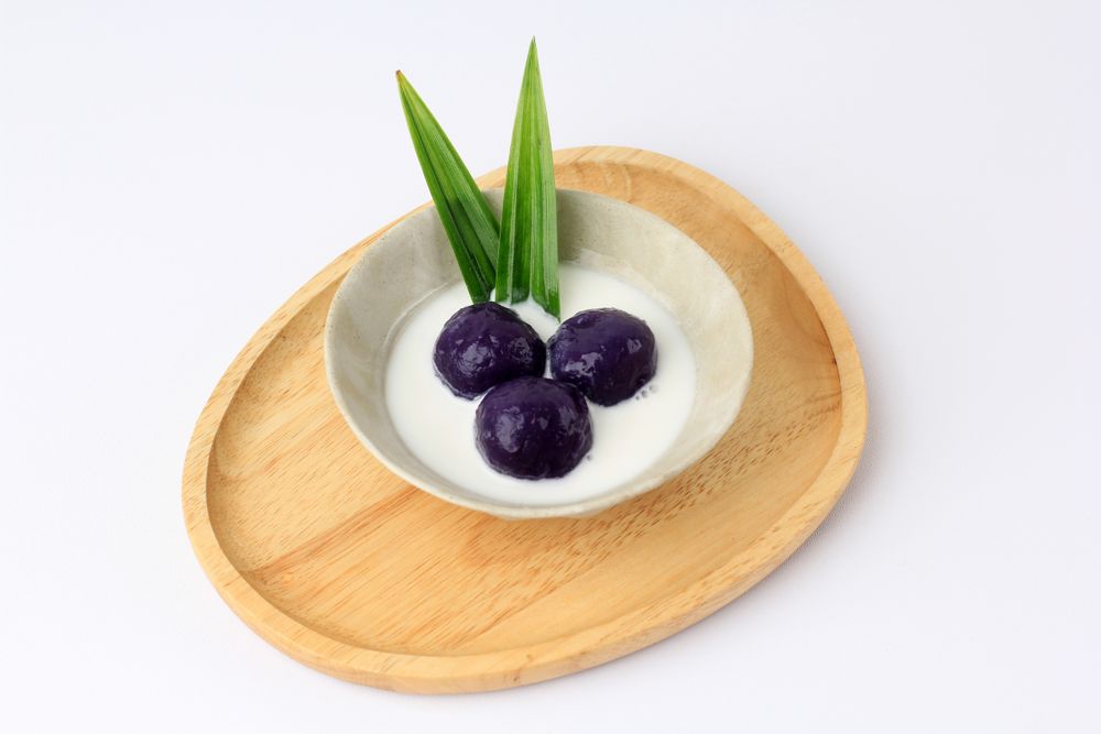 Bowl of 3 purple sweet potato balls covered in coconut milk sauce