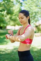 A woman wearing a fitness tracker is exercising in a park, emphasizing her focus on health and wellness
