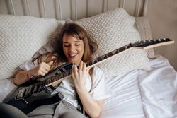 Young brunette woman playing guitar on bed