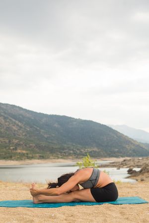 Woman practicing yoga outdoors near water