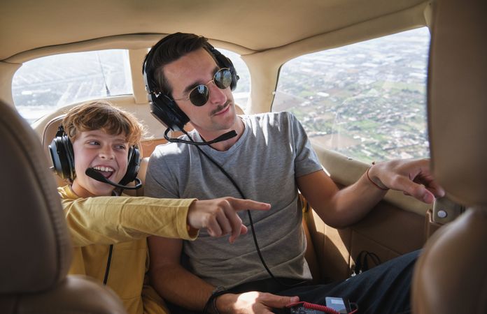 Cheerful kid with father pointing away during flight in airplane