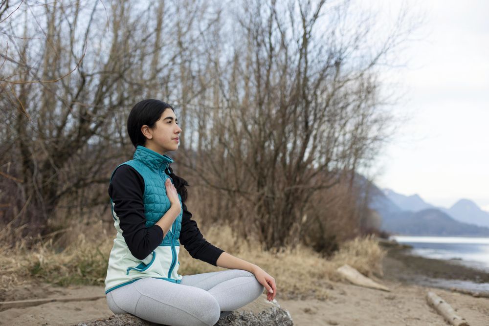 Young female sitting on a log while meditating near a lake
