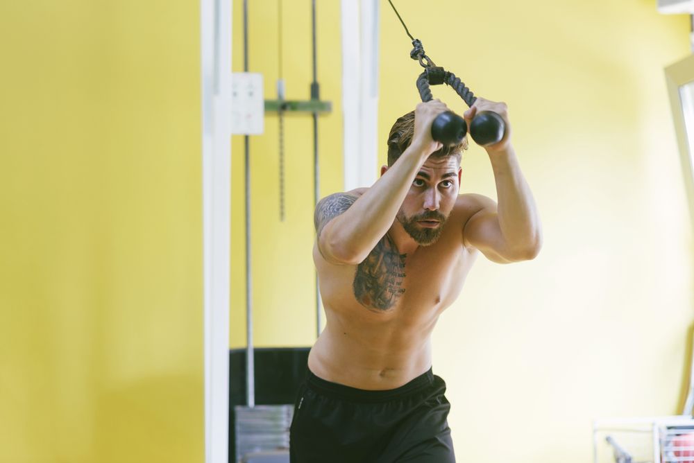 Tattooed male in gym working out his arms using weights machine