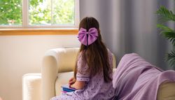 Young girl looking out window, wearing purple bow.