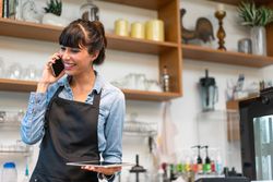 Female speaking on phone working in cafe with digital tablet in hand