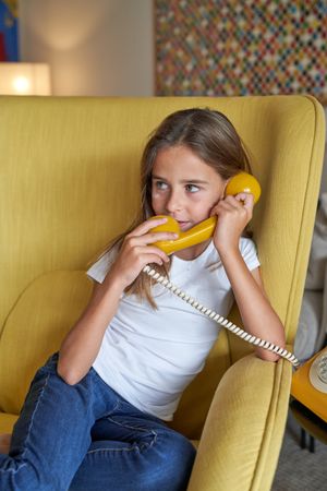 Girl holding handset of yellow telephone