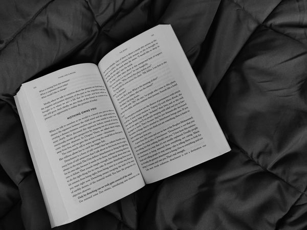 Greyscale photo of open book on bed
