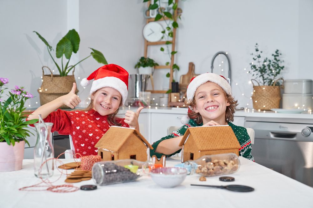 Happy children decorating gingerbread houses in kitchen