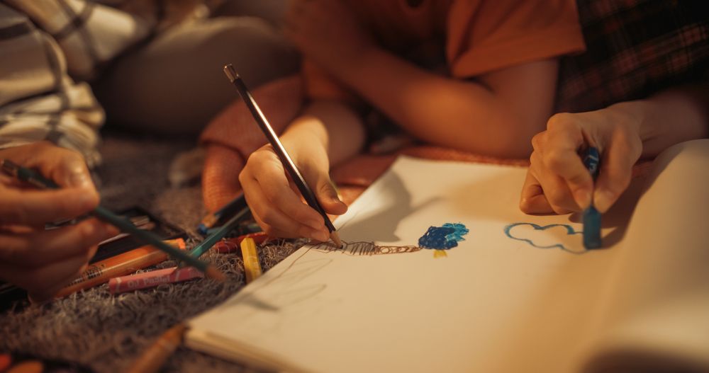 Close Up On Hands Of Happy Korean Family Drawing Together in Notebook With Pens And Pencils.