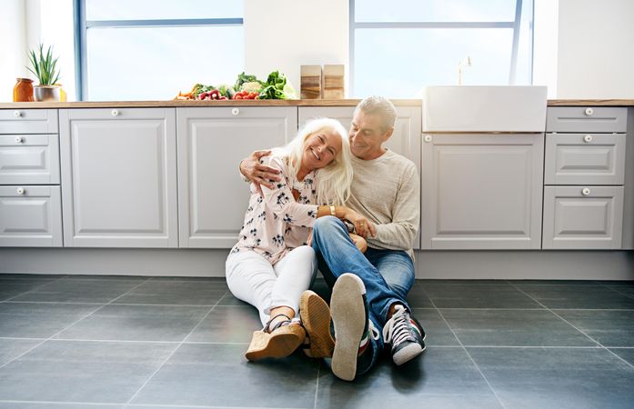 Older smiling couple on the floor of their bright kitchen