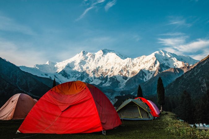Red tents camping facing snow capped mountains in Pakistan