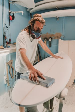 Man in respirator polishing surf board in workshop