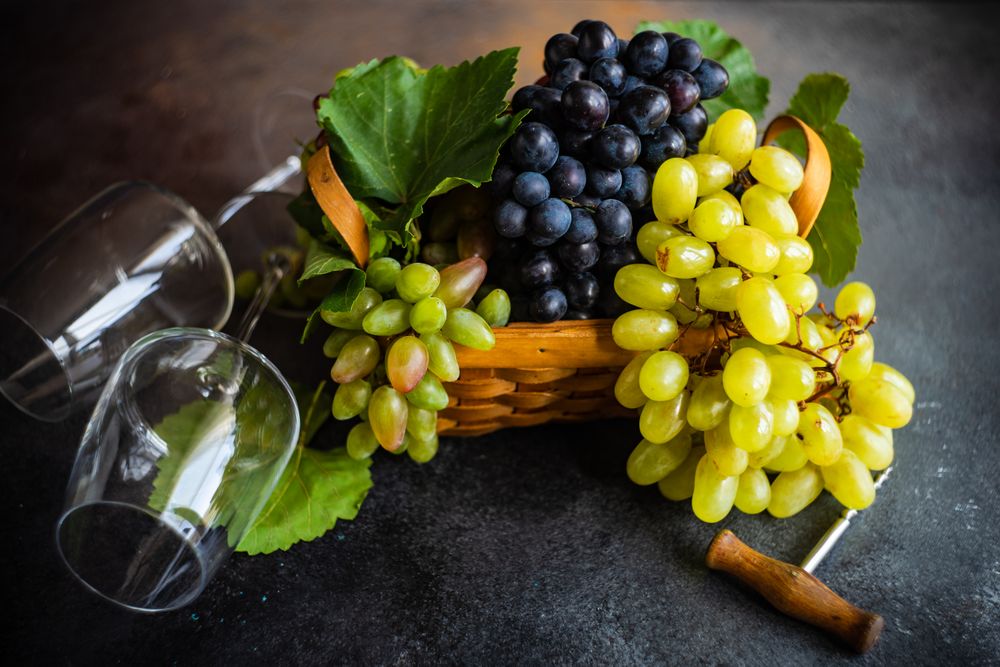 Box of fresh green & red grapes on grey kitchen counter with two wine glasses