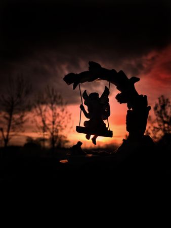 Silhouette of child riding swing during sunset