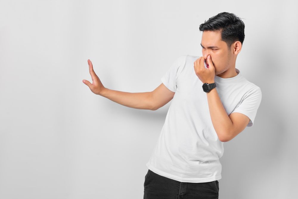 Asian male in grey studio gesturing something smells bad