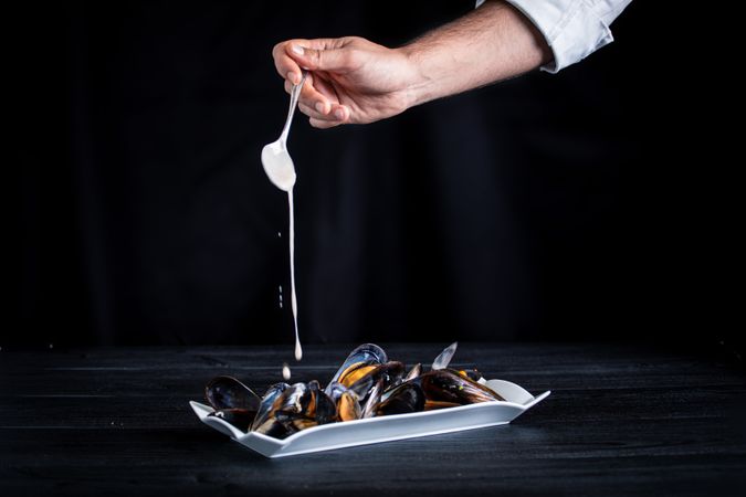 Person pouring fresh tasty mussels with Thai sauce