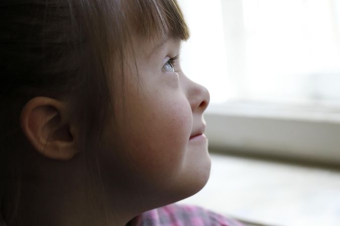 Close up portrait of little girl with Down syndrome looking out a window