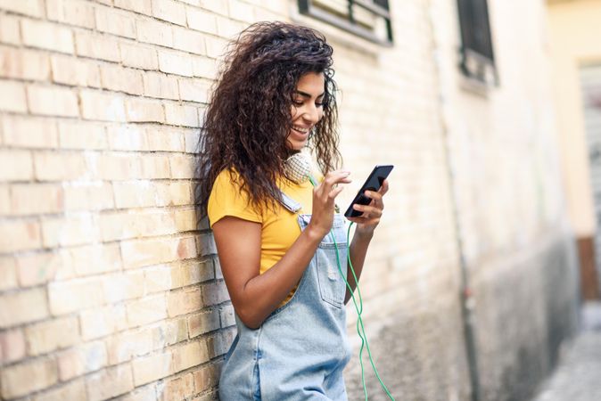 Arab woman texting with her smart phone leaning on brick wall