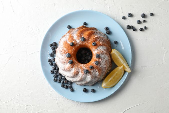 Cake with powdered sugar, blueberry and lemon on plain background, copy space