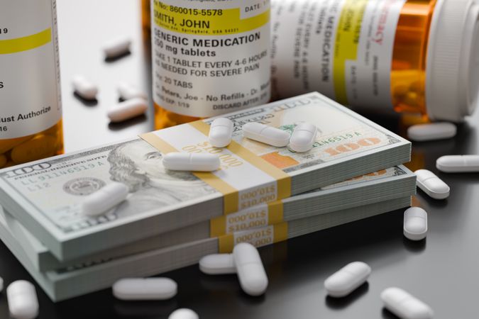 Prescription Medicine Bottles and Pills Next To Stacks of 100 Dollar Bills.