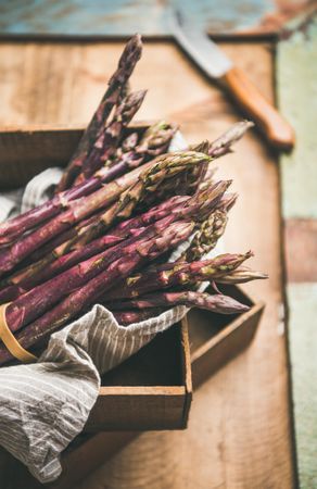 Close up of bunches of purple asparagus, knife one wooden background, vertical composition