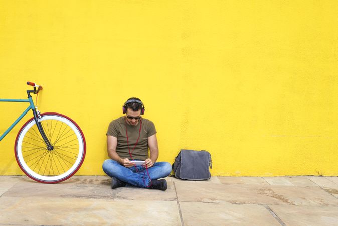 Man with red headphones sitting outside looking at phone