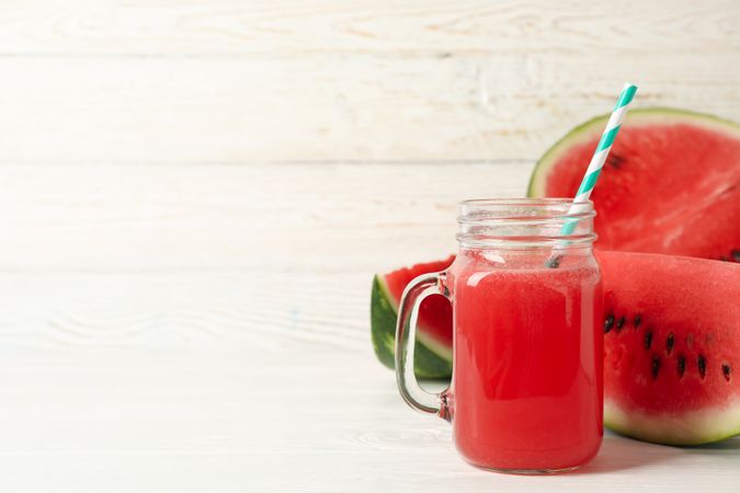 Glass jar of watermelon juice and slices on wooden background