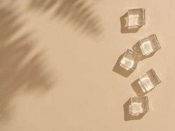 Flat lay of ice cubes on beige background with shadow of leaves