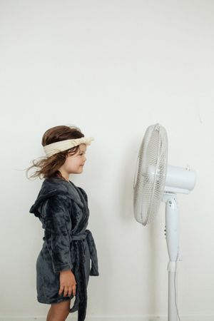 Little girl standing against fan at home